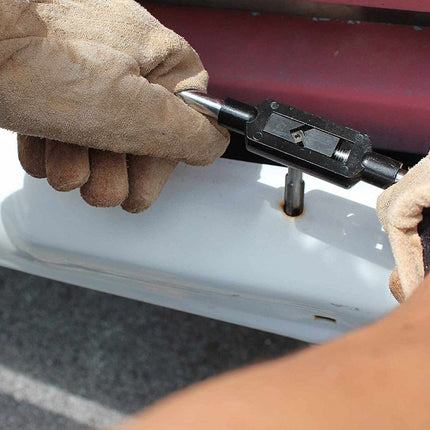 Close-up of a person wearing tan leather work gloves using a black metal tool on a white vehicle door next to a dark red body panel.