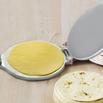  Tortilla press with a tortilla inside and a stack of tortillas on a wooden surface.