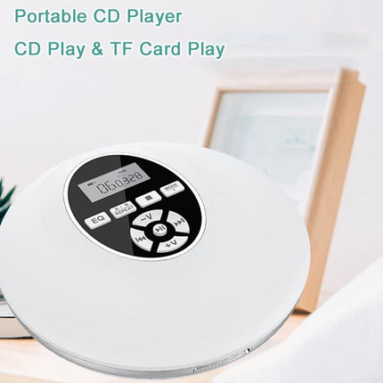 A white portable CD player with a digital display screen and control buttons, shown on a light wooden surface with a blurred framed picture and small plant in the background. Text at the top reads 'Portable CD Player CD Play & TF Card Play'.