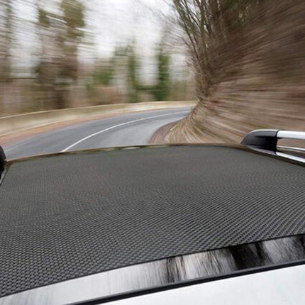 Car roof with a black carbon fiber pattern driving on a road with trees.