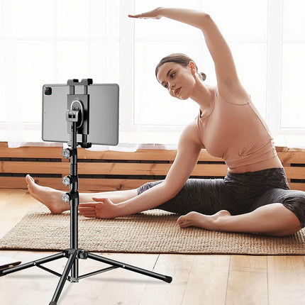 Woman stretching on a mat with a tablet on a stand in front of her