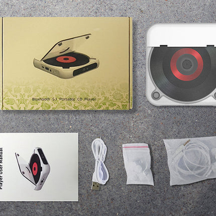 Portable CD player with packaging, user manual, USB cable, and cleaning kit on a gray surface.