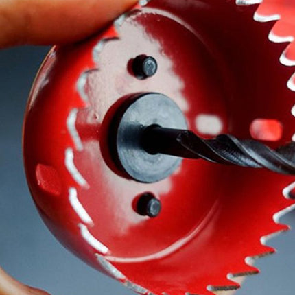 Red circular saw blade with a drill bit attached, held by a hand against a gray background.