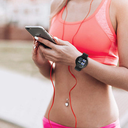 Person wearing a smartwatch and holding a phone with red earbuds, outdoors.