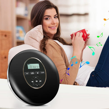 A round black portable CD player with a digital display sits on a white table in the foreground, while a woman relaxes on a couch in the background holding a red mug, with colorful music notes floating around.