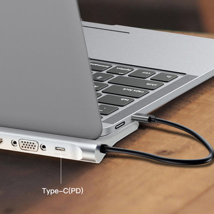 A close-up of a silver laptop on a wooden surface, showing a black Type-C PD cable plugged into the laptop's side port.