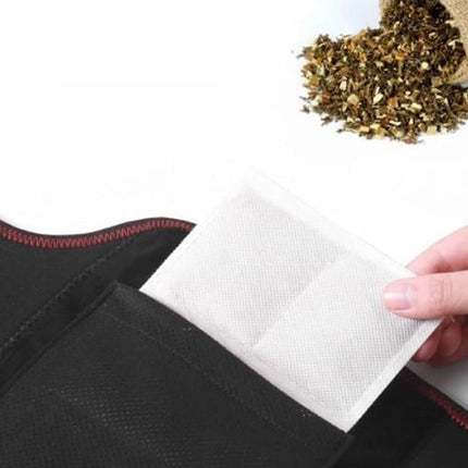 Hand placing a white sachet into a black bag with dried herbs on a white background